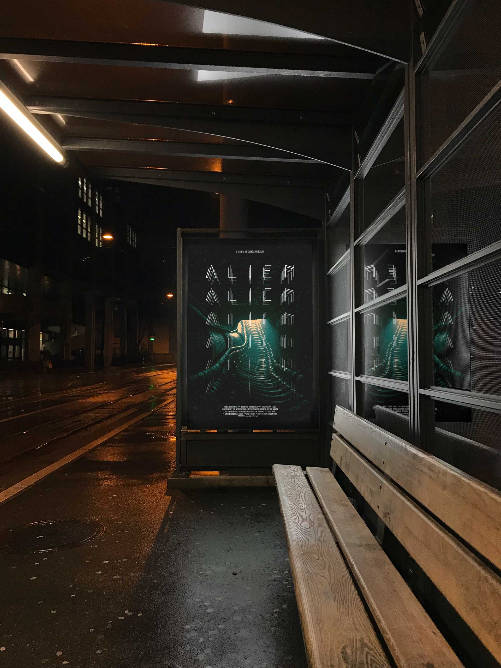 A movie poster that reads "Alien" mounted behind a bus shelter billboard along a city street, with street lights reflecting off the glass.