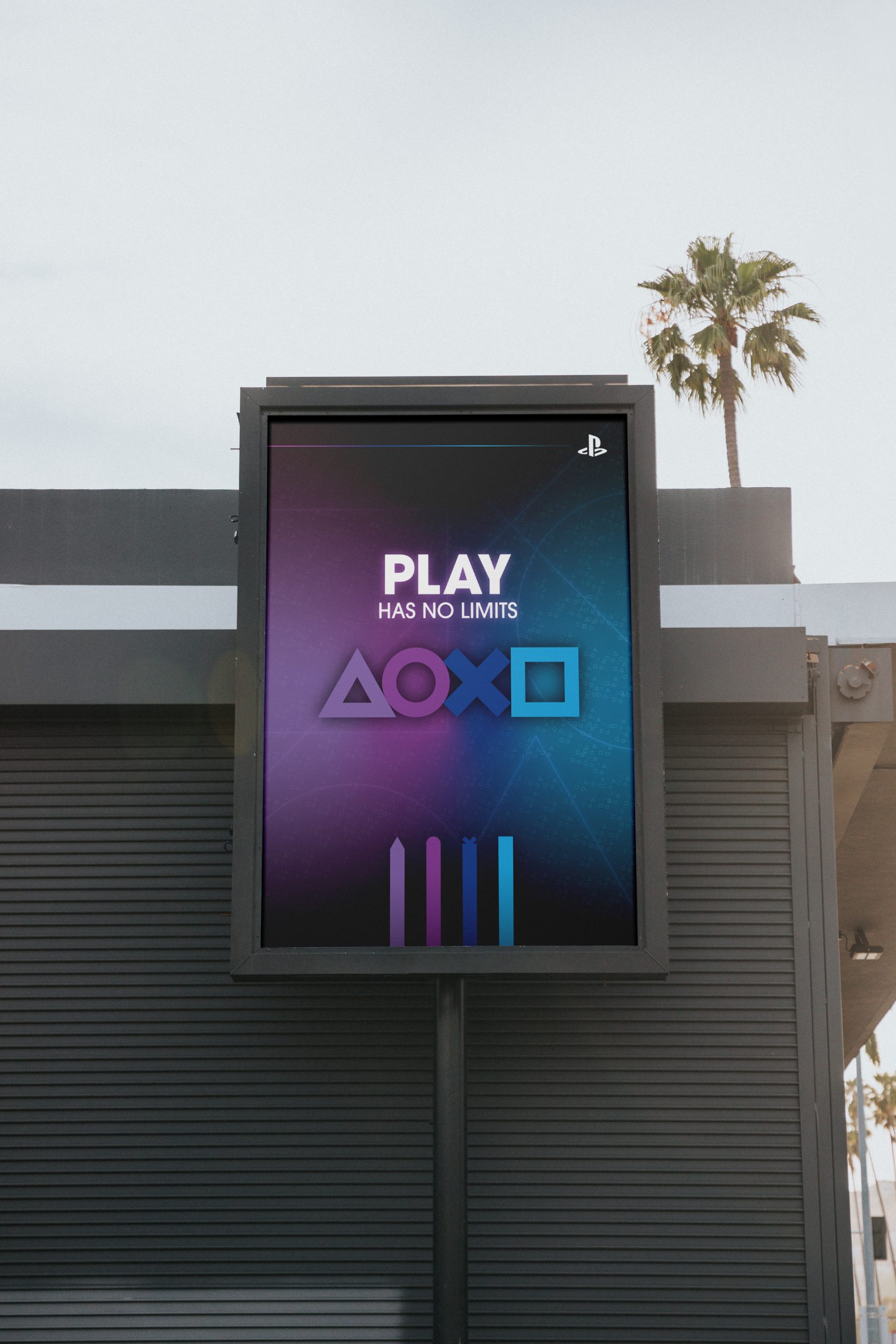 "Play Has No Limits" poster inspired by PlayStation A gaming poster for PlayStation that features the 4 brand icons (triangle, circle, x, and square) in that order, the slogan "Play Has No Limits", and the PlayStation logo on a blue/purple/pink gradient background. Poster is mounted off the side of a small building on a black billboard during the summer time, with a palm tree unfocused in the background.