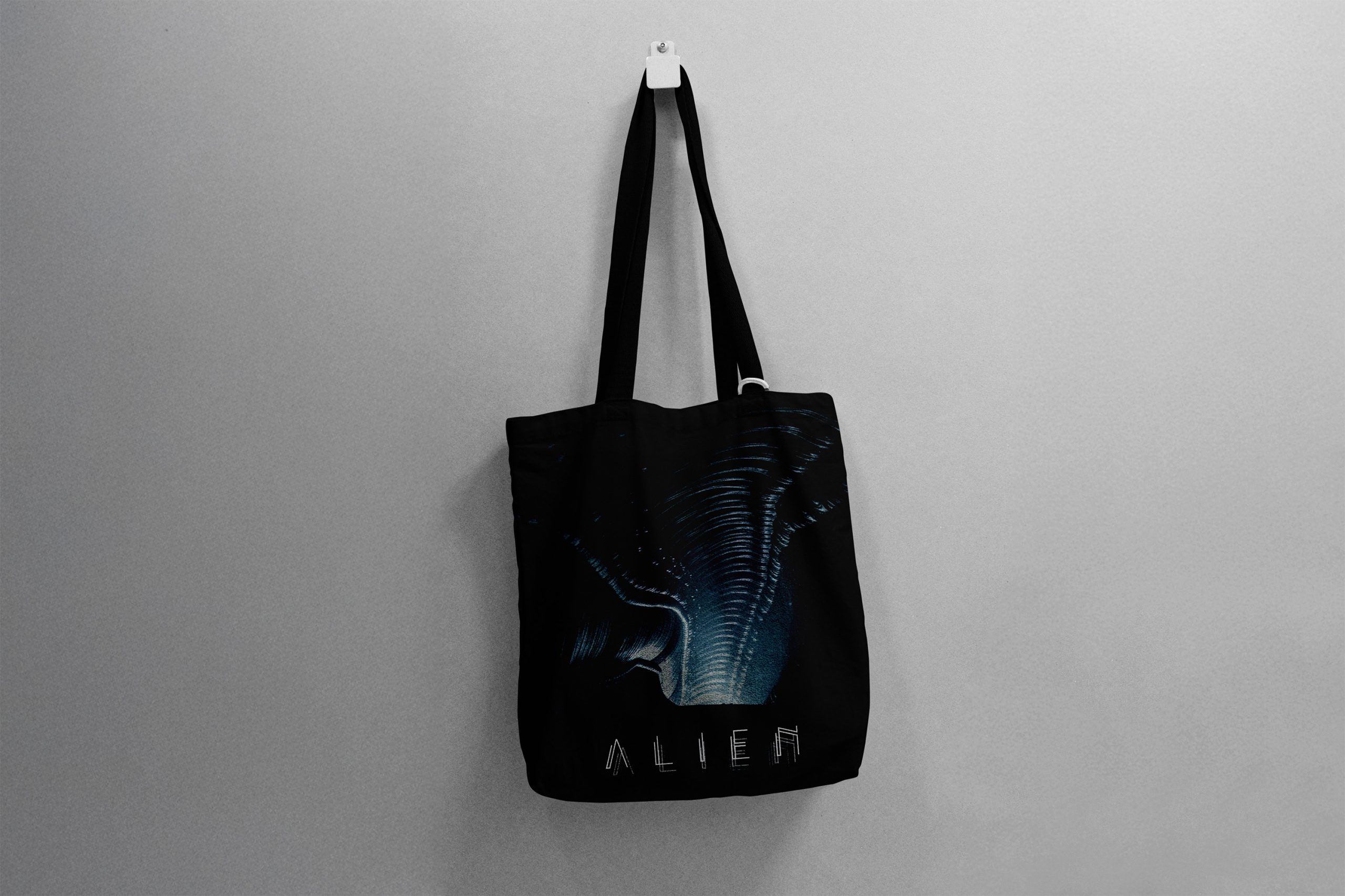 Dark tote bag that says "Alien" below a dark corridor, hung up on a white wall